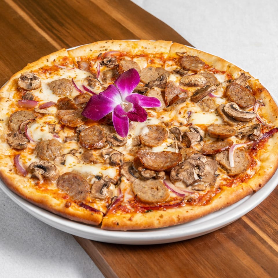Mona Lisa Cucina's sausage, mushroom, and red onion pizza, garnished with a purple orchid.