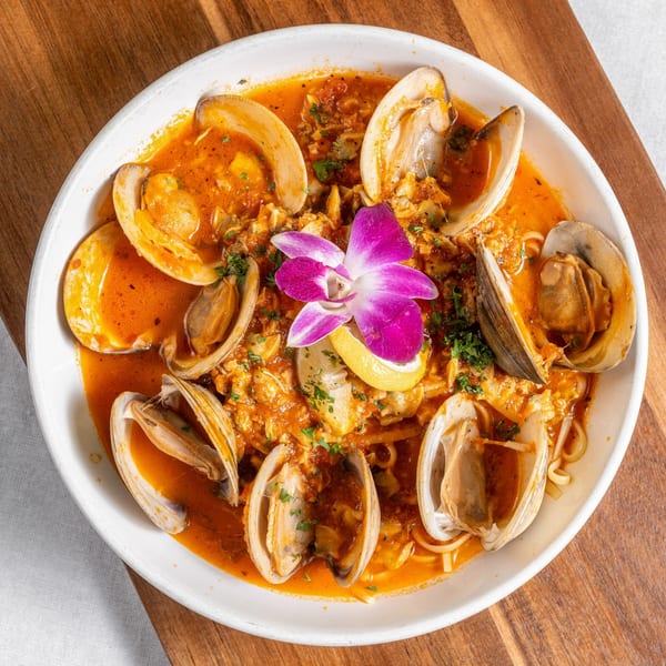 Clams in red sauce with pasta, garnished with a lemon wedge and purple orchid.
