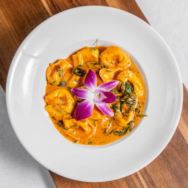 Mona Lisa Cucina's tortellini pasta in a creamy orange sauce, garnished with a purple orchid.
