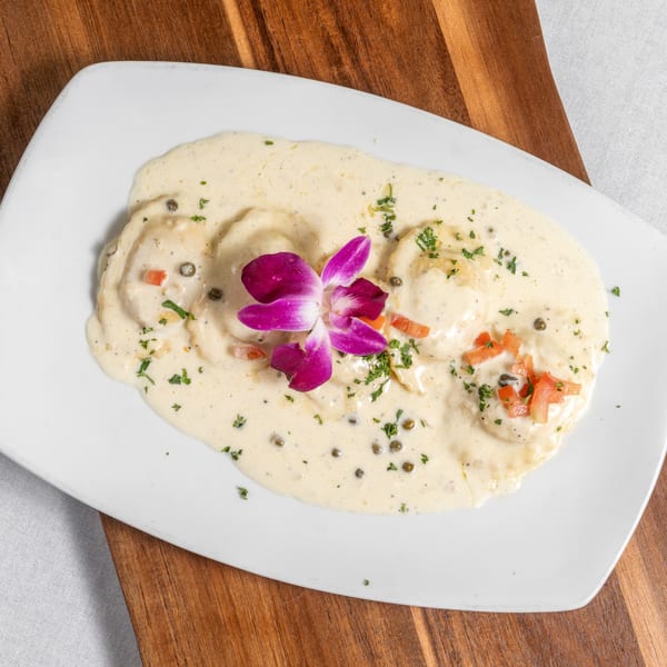 Ravioli in a creamy white sauce, garnished with a purple orchid, capers, and diced tomatoes.