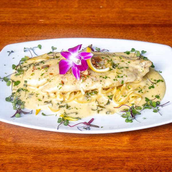 Mona Lisa Cucina's creamy pasta dish with fish, garnished with a purple orchid and lemon.