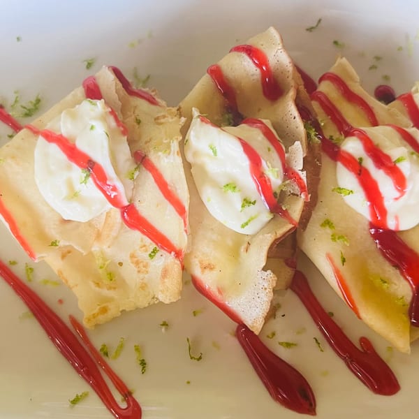 Three folded crepes topped with white cream, red drizzle, and green zest on a white plate.