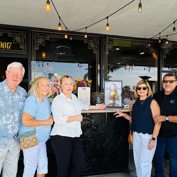 Five people, including a restaurant worker, pose outside a restaurant entrance with string lights and flowers.