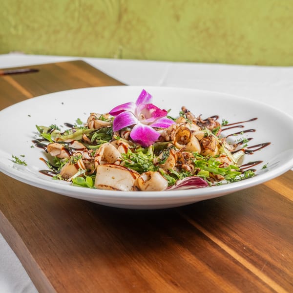 Grilled calamari salad with mixed greens, balsamic glaze, and a purple orchid garnish.