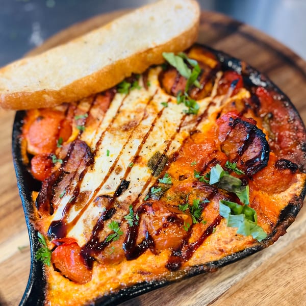 Baked feta with cherry tomatoes, sausage, and herbs, drizzled with balsamic glaze, served with toast.