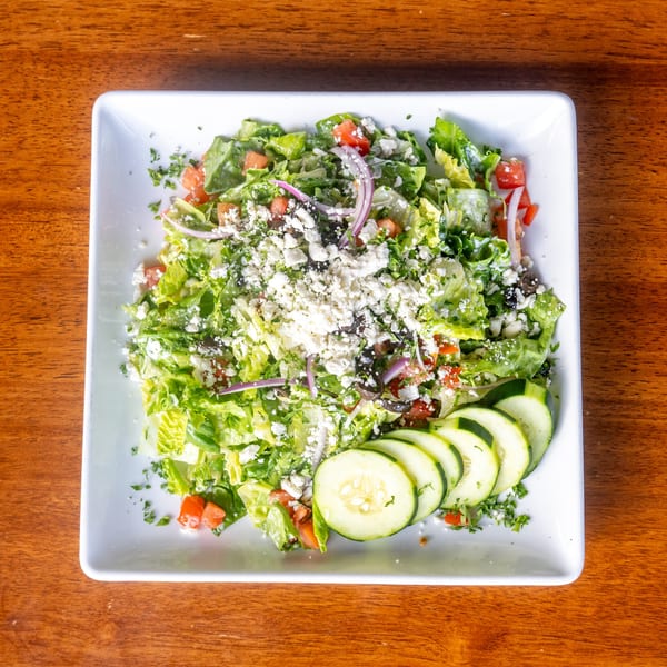 A Mona Lisa Cucina salad with lettuce, tomatoes, red onions, feta cheese, and cucumber slices.