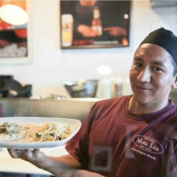 A Mona Lisa Cucina staff member in a black cap and red shirt holds a plate of pasta.
