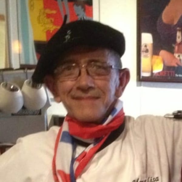 Smiling man in a black beret and red, white, and blue scarf, wearing a Mona Lisa Cucina shirt.