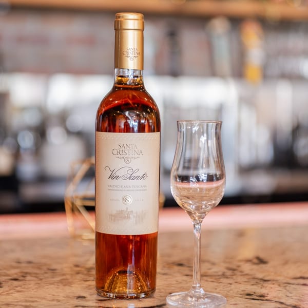 A bottle of Santa Cristina Vin Santo dessert wine next to an empty tasting glass on a counter.