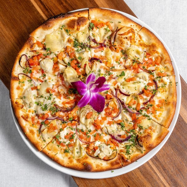Mona Lisa Cucina's white pizza with artichokes, red onions, tomatoes, and a purple orchid garnish.