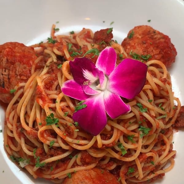 Spaghetti with meatballs and red sauce, garnished with parsley and a pink orchid.