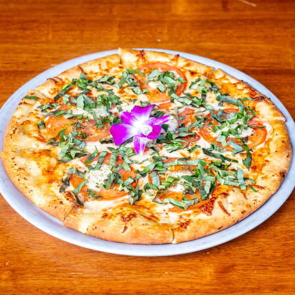Mona Lisa Cucina's Margherita pizza, topped with fresh basil, sliced tomatoes, and a purple orchid.