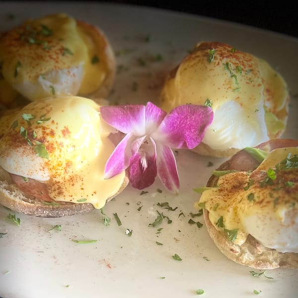 Four eggs Benedict with hollandaise sauce, paprika, and parsley, garnished with a purple orchid.