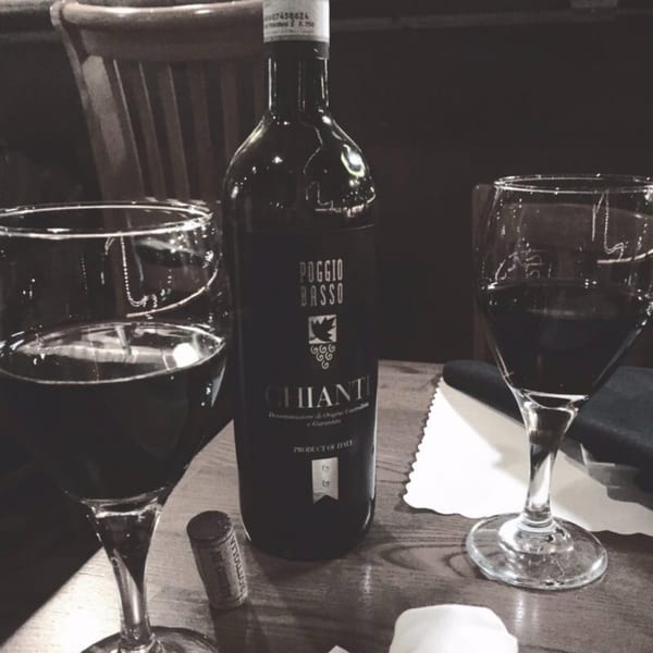 A bottle of Poggio Basso Chianti wine with two full wine glasses on a table.