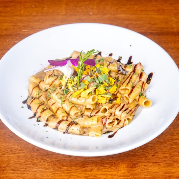 Rigatoni pasta in a creamy sauce with balsamic glaze, garnished with edible flowers and herbs.