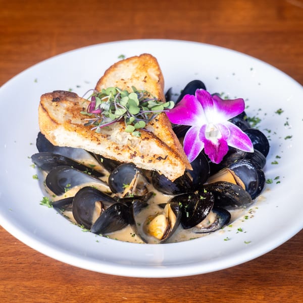 Mona Lisa Cucina's mussels in a creamy sauce, topped with toasted bread, microgreens, and an orchid.