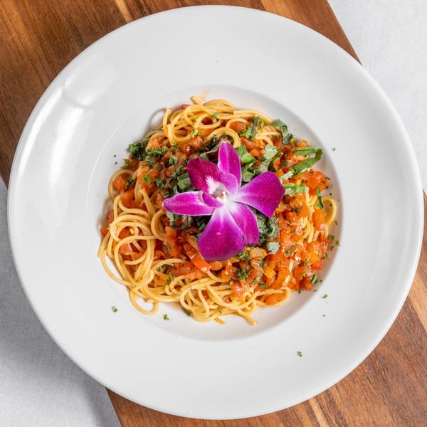 Mona Lisa Cucina's spaghetti with tomato sauce, fresh herbs, and a purple orchid garnish.