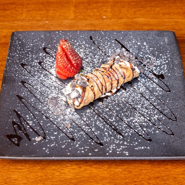 Mona Lisa Cucina's cannoli, drizzled with chocolate and powdered sugar, served with a fresh strawberry.