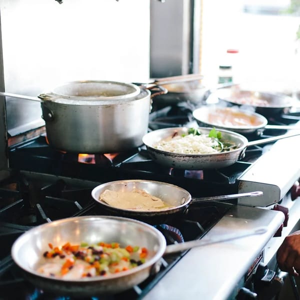 Multiple pans and a pot cooking on a commercial stove, preparing Italian dishes.