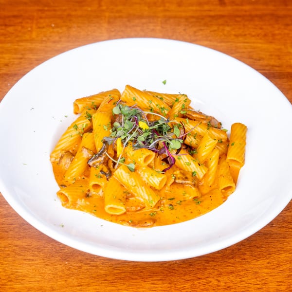 Rigatoni pasta in a creamy orange sauce with mushrooms, garnished with microgreens and herbs.