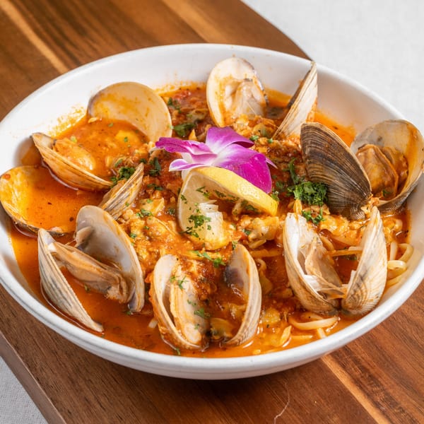 Clams in a rich red sauce with pasta, garnished with a lemon slice and purple orchid.
