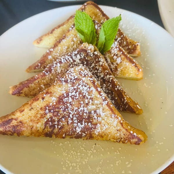 Four triangular French toast slices, dusted with powdered sugar and garnished with fresh mint sprigs.