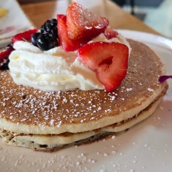 Fluffy pancakes topped with whipped cream, fresh strawberries, blueberries, and powdered sugar.