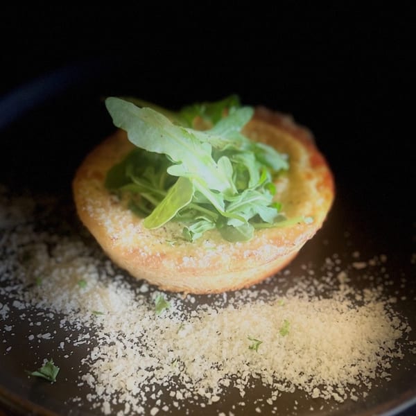 A golden-brown pastry cup filled with fresh green arugula and sprinkled with white cheese.