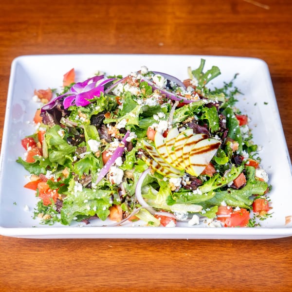 A vibrant Mona Lisa Cucina house salad with mixed greens, tomatoes, onions, cheese, and a purple orchid.