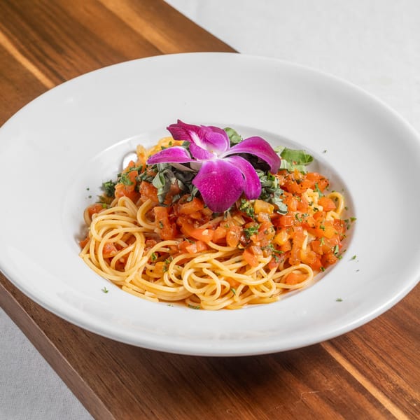Spaghetti with diced tomatoes, herbs, and a purple orchid garnish in a white bowl.