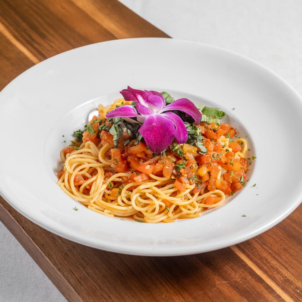 Spaghetti with diced tomatoes, herbs, and a purple orchid garnish in a white bowl.