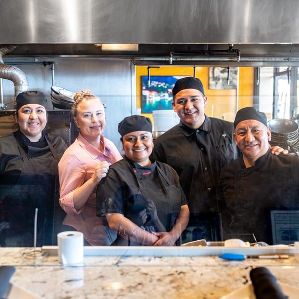 Five Mona Lisa Cucina chefs and kitchen staff smiling behind a counter in the kitchen.
